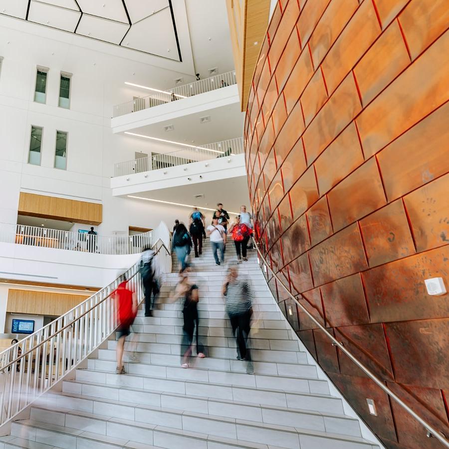 university hall interior showing students walking in blurred motion up and down the main entrance stairs